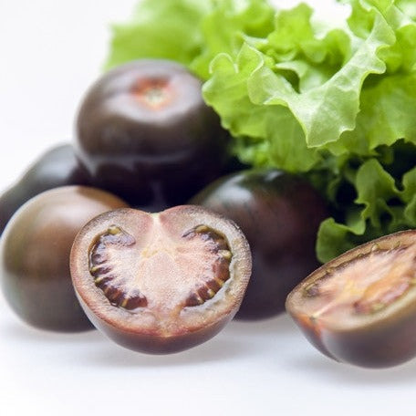 Close-up of whole and halved Black Cherry Tomatoes with green lettuce leaves in the background