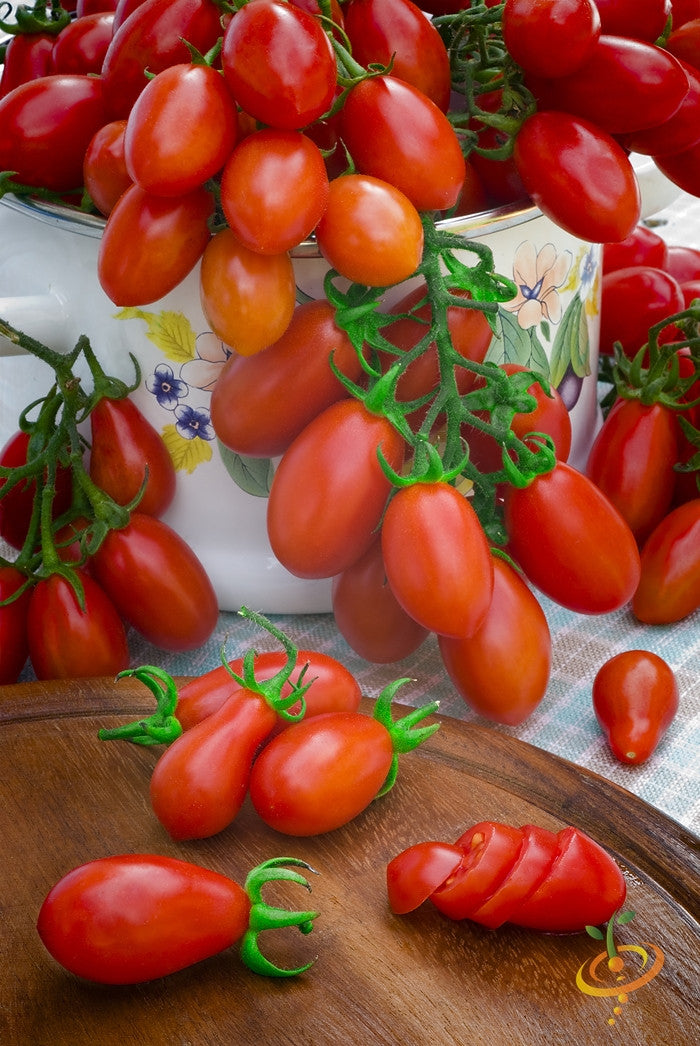 Cluster of ripe red pear tomatoes with one sliced on a wooden board and a decorative cup in the background